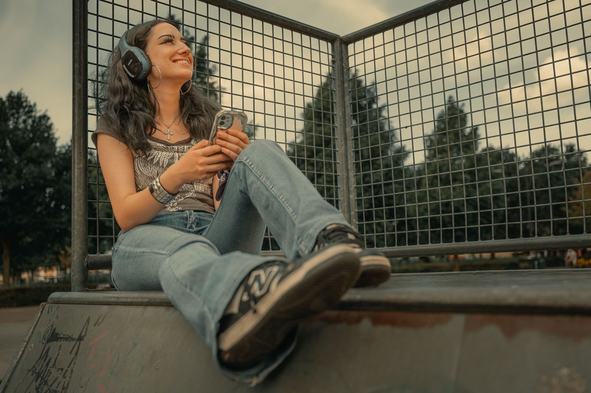 Jonge vrouw met stoere kleding, een koptelefoon en een mobieltje op een skatebaan.