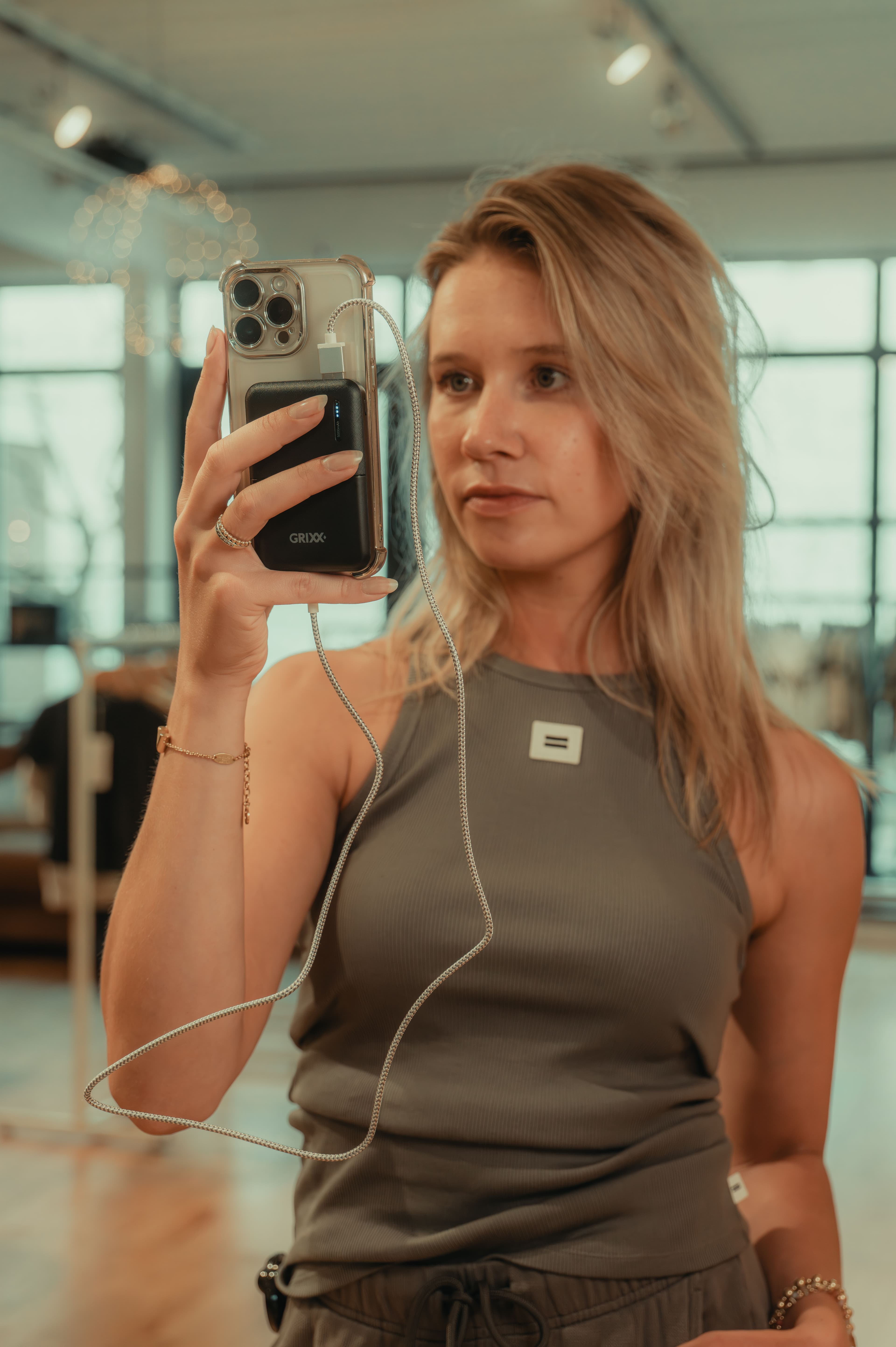 Knappe blonde vrouw met pokerbank en mobieltje voor passpiegel in kledingwinkel.